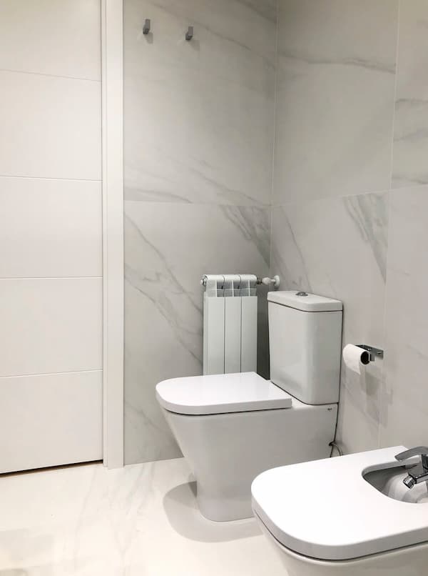 Reforma de baño con paredes de con azulejos de grandes dimensiones con texturas que parecen marmol, puertas de baño blancas y suelo blanco