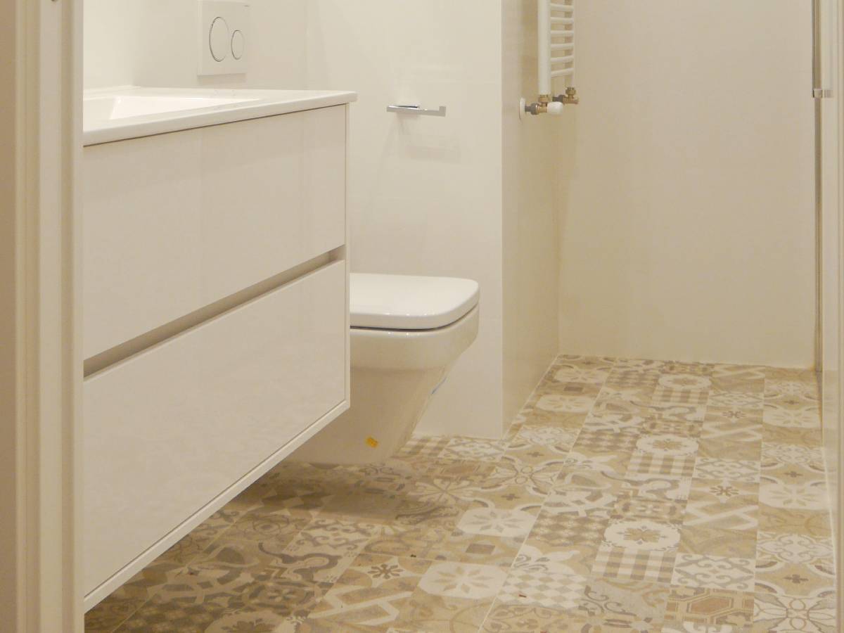 Baño reformado: suelo de azulejos con diferentes dibujos pero todos con mismos tonos suaves, mobiliario y sanitarios suspendidos, tonos blancos cálidos